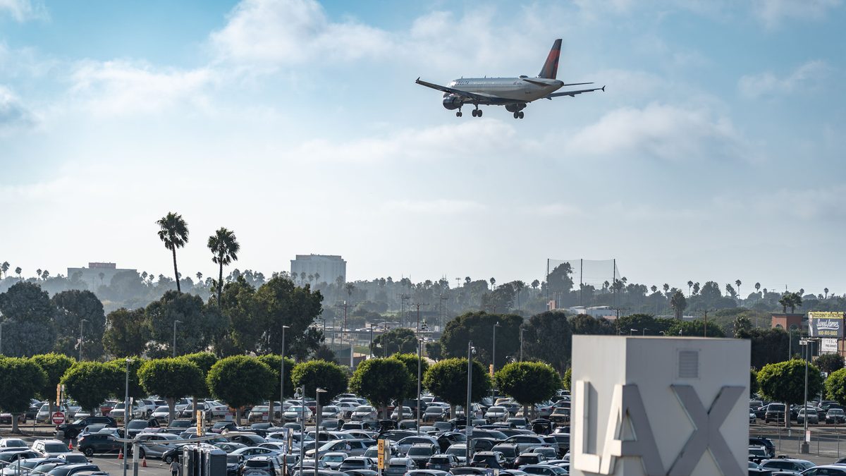Airplane flying over a busy LAX parking area