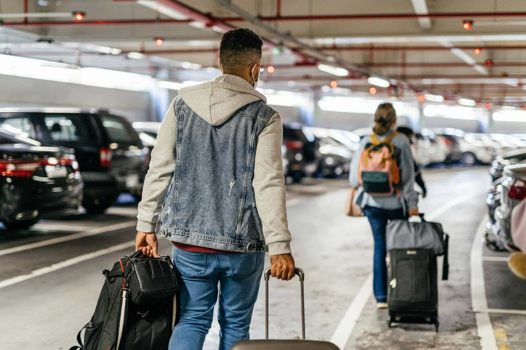 Passengers walking with luggage through covered airport parking garage