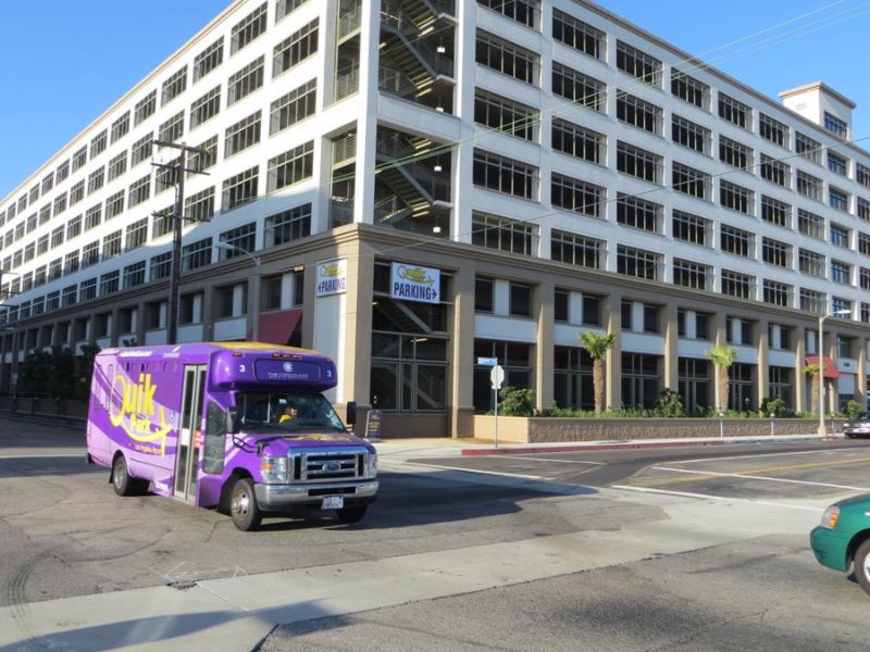 QuikPark LAX shuttle driving past a covered parking garage