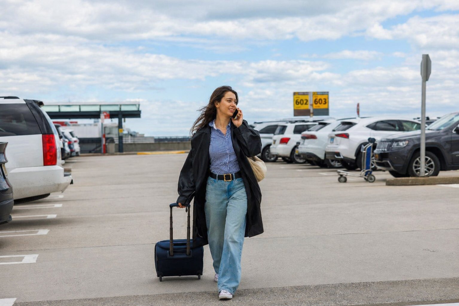 Woman walking through airport parking lot with suitcase before flight