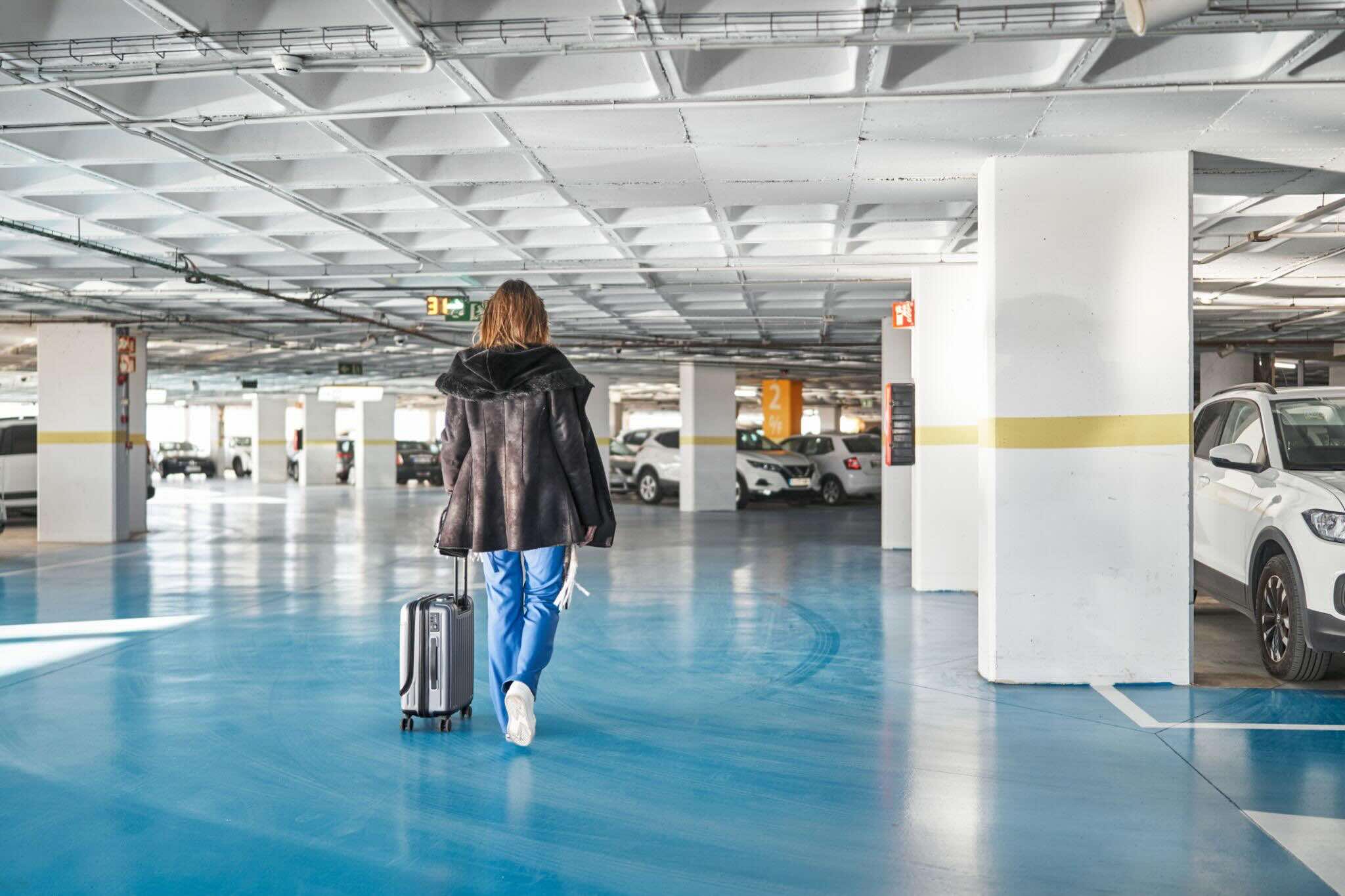 traveler walking through covered parking garage with luggage